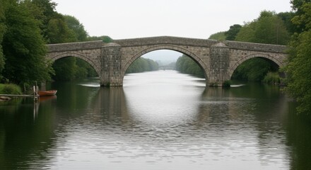 Fototapeta premium Stone Bridge Spanning River Amidst Lush Greenery and Overcast Sky.