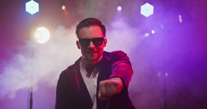 Dancer showman entertainer man performer dance on stage. Vibrant nightclub lights pierce smoke as he grooves in a velvet jacket and sunglasses. Bold energy and charismatic performance.