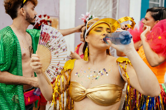 Woman drinking water during carnival street festival, showing hydration, health and self care during summer celebration