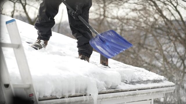 Contractor shovels heavy snow off a residential roof to reduce ice dams, protect gutters, and prevent winter storm damage to a home. 15038