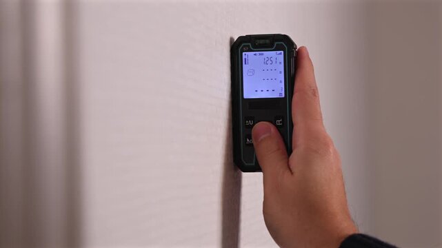 Une personne utilisant un t&eacute;l&eacute;m&egrave;tre laser pour mesurer la surface d'un bien immobilier.