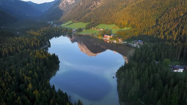 Aerial view of the Hintersee lake reflecting the mountains, framed by dark green forests and illuminated by the warm glow of the sun, Ramsau bei Berchtesgaden, Bavaria, Germany.
