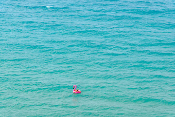 Person relaxing on pink flamingo inflatable ring in turquoise sea water Crete Greece