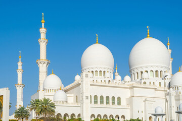Fototapeta premium White domes and tall minarets of the Sheikh Zayed Grand Mosque against clear blue sky in Abu Dhabi, United Arab Emirates. Islamic architecture. Travel and tourism in UAE