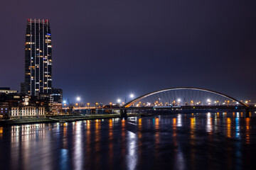 Obraz premium Panorama of Bratislava with illuminated modern buildings on the banks of the Danube and a bridge over the river - against the background of a dark evening sky