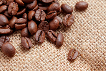 Fototapeta premium Cracked roasted coffee beans scattered on coarse textured burlap fabric. Aromatic caffeine beverage concept.