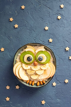 Creative owl design made with fruit arranged on a bowl placed on a blue surface with star confetti around