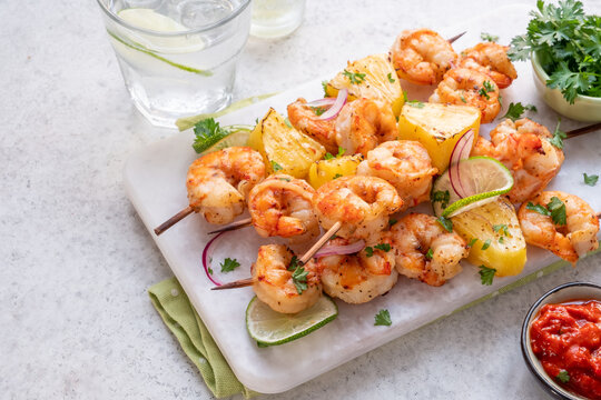Shrimp skewers with pineapple and lime served with salsa on a white platter