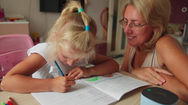 Mother helps her young daughter with written exercises at a desk. Preparing for school by developing focus and basic learning skills