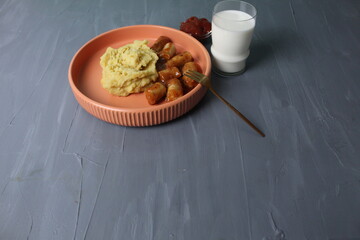Fototapeta premium lunch sausages with tomato sauce and side dish mashed potatoes glass of milk on a gray background with space for text copyspace