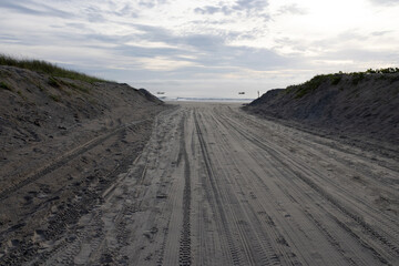 A sandy road leads to the beach; on either side of the road rises a sand wall about two meters high