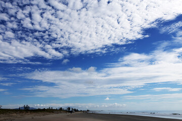 Beautiful coastal landscape composed of a long stretch of sand with the sea to the right; the image is divided in a way that shows much more of the sky