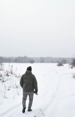 Man walking through a snowy winter landscape with a camera in hand, outdoor photographer in cold weather, minimal scene with falling snow and copy space.
