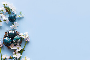 Easter flat lay. Stylish easter eggs in nest and cherry flowers on blue background. Easter celebration, season greetings mockup. Spring modern floral banner © sonyachny
