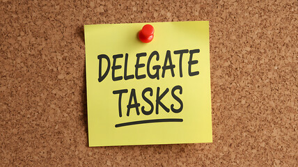Delegate Tasks Sticky Note on Cork Bulletin Board with Red Pin, Reminder for Productivity and Time Management