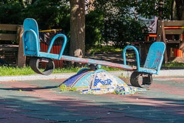Vibrant childrens playground with a blue and green merry-go-round, patterned tile mosaic floor, wooden bench in background, natural lighting
