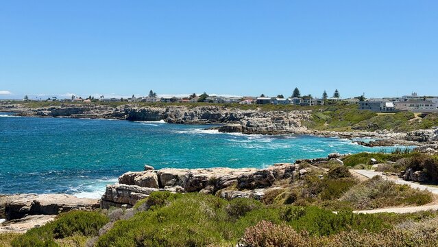 Walking along the coastal shore between Hermanus town center and the harbor, turquoise blue sea, warm sunshine and summer holiday atmosphere in South Africa.