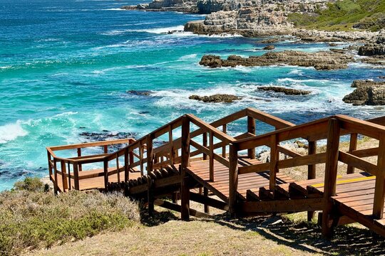 Walking along the coastal shore between Hermanus town center and the harbor, turquoise blue sea, warm sunshine and summer holiday atmosphere in South Africa.