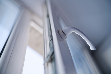 Detail of a white PVC window handle mechanism. Modern double glazing frame opened slightly for ventilation. Interior hardware fittings and home renovation. Photo © slexp880