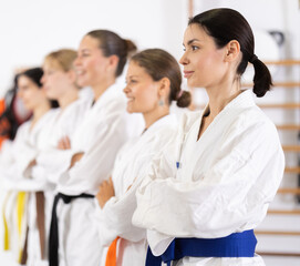 Fototapeta premium Female team of young martial arts athletes is standing in gym, public shoot, sports training camps. Preparation for competitions, sports as way of life.........