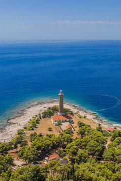 Aerial view of the Veli Rat Lighthouse stands tall against the deep blue Adriatic Sea, its stark white contrasting with the rugged coastline, Veli Rat, Zadar County, Croatia.