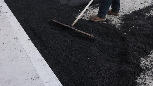Worker uses rake to level freshly laid asphalt on road process takes place in an urban area
