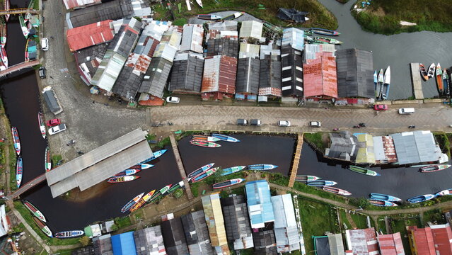 Aerial top-down view of a riverside village at Laguna de la Cocha, Colombia. Boats moored along a winding waterway with colorful houses surrounded by lush vegetation.