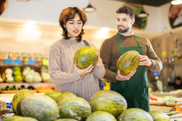 Fototapeta premium Polite young male seller offering melon to girl standing by product stand in grocery store