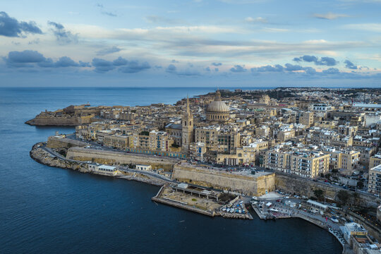 Aerial view of ancient stone fortifications meeting the turquoise sea, the dome of St. Paul's Cathedral rising above the historic skyline, Valletta, Sliema, Malta.