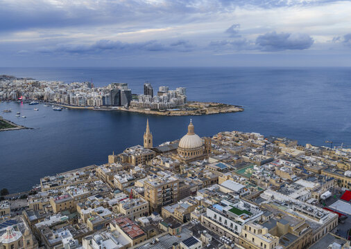 Aerial view of the iconic dome of Saint Paul's Cathedral rises majestically over a dense urban landscape, framed by the deep blue sea, Valletta, Sliema, Malta.