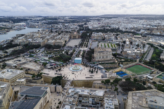 Aerial view of a bustling city square with the iconic Triton Fountain and the grand buildings, framed by the azure waters of the harbor, Valletta, Sliema, Malta.