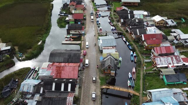 Cinematic drone view of a remote community at Laguna de la Cocha, with boats, wooden docks and homes built along the lagoon in a natural setting.