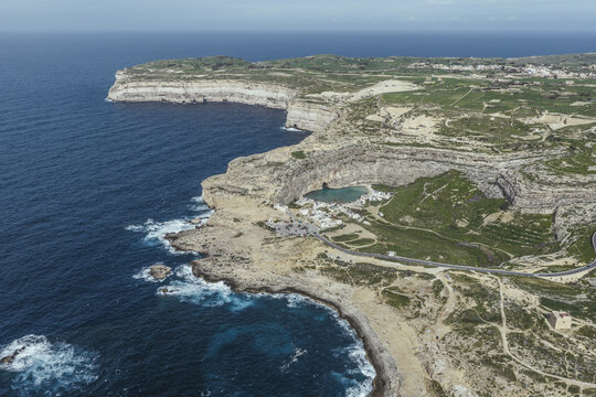 Aerial view of the rugged Dwejra Bay coastline where the azure sea clashes with the rocky cliffs, San Lawrenz, Malta.