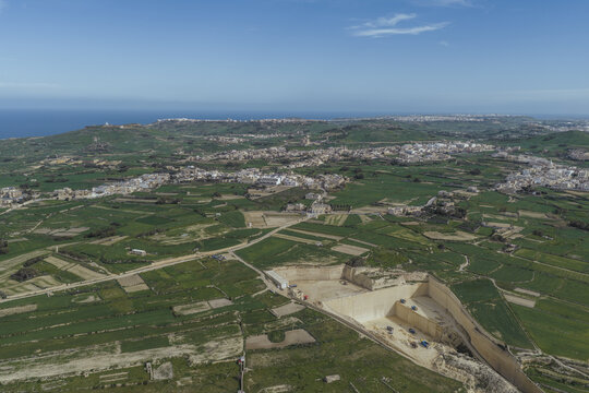 Aerial view of verdant fields meet the rugged coastline, where the azure sea kisses the land, Dwejra Bay, San Lawrenz, Malta.