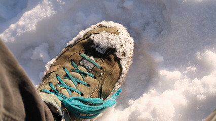 Obraz premium Worn hiking boot with teal laces partially covered in snow on sunlit winter ground