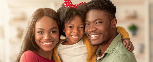Family stands together in a bright living room. The parents smile widely, while the child in the middle beams with joy. This moment captures their love and togetherness. © Prostock-studio