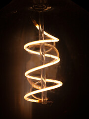 Macro view of a glowing yellow LED spiral inside a decorative bulb.