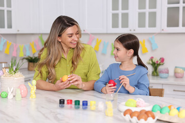 Naklejka premium Easter celebration. Mother and her daughter painting eggs at white marble table in kitchen