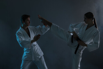 Man and woman in uniforms practicing karate on dark background with smoke © New Africa