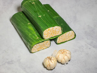 Tempeh wrapped in banana leaves with a marble background. Tempeh is a traditional Indonesian food made from soybeans. It is beneficial for health.