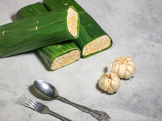Tempeh wrapped in banana leaves with a marble background. Tempeh is a traditional Indonesian food made from soybeans. It is beneficial for health.