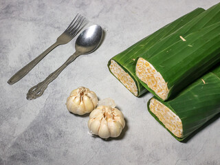Tempeh wrapped in banana leaves with a marble background. Tempeh is a traditional Indonesian food made from soybeans. It is beneficial for health.