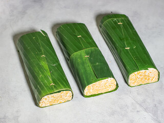 Tempeh wrapped in banana leaves with a marble background. Tempeh is a traditional Indonesian food made from soybeans. It is beneficial for health.