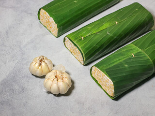 Tempeh wrapped in banana leaves with a marble background. Tempeh is a traditional Indonesian food made from soybeans. It is beneficial for health.