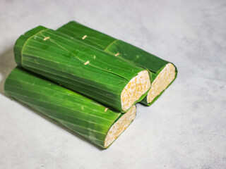 Tempeh wrapped in banana leaves with a marble background. Tempeh is a traditional Indonesian food made from soybeans. It is beneficial for health.