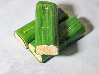 Tempeh wrapped in banana leaves with a marble background. Tempeh is a traditional Indonesian food made from soybeans. It is beneficial for health.