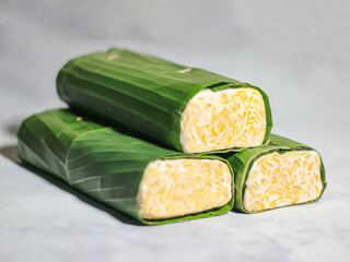 Tempeh wrapped in banana leaves with a marble background. Tempeh is a traditional Indonesian food made from soybeans. It is beneficial for health.