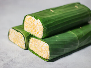 Tempeh wrapped in banana leaves with a marble background. Tempeh is a traditional Indonesian food made from soybeans. It is beneficial for health.