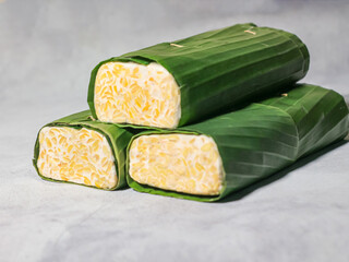 Tempeh wrapped in banana leaves with a marble background. Tempeh is a traditional Indonesian food made from soybeans. It is beneficial for health.