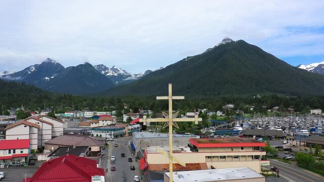 Aerial drone view flying past an orthodox cross on a steeple revealing the city of sitka, alaska